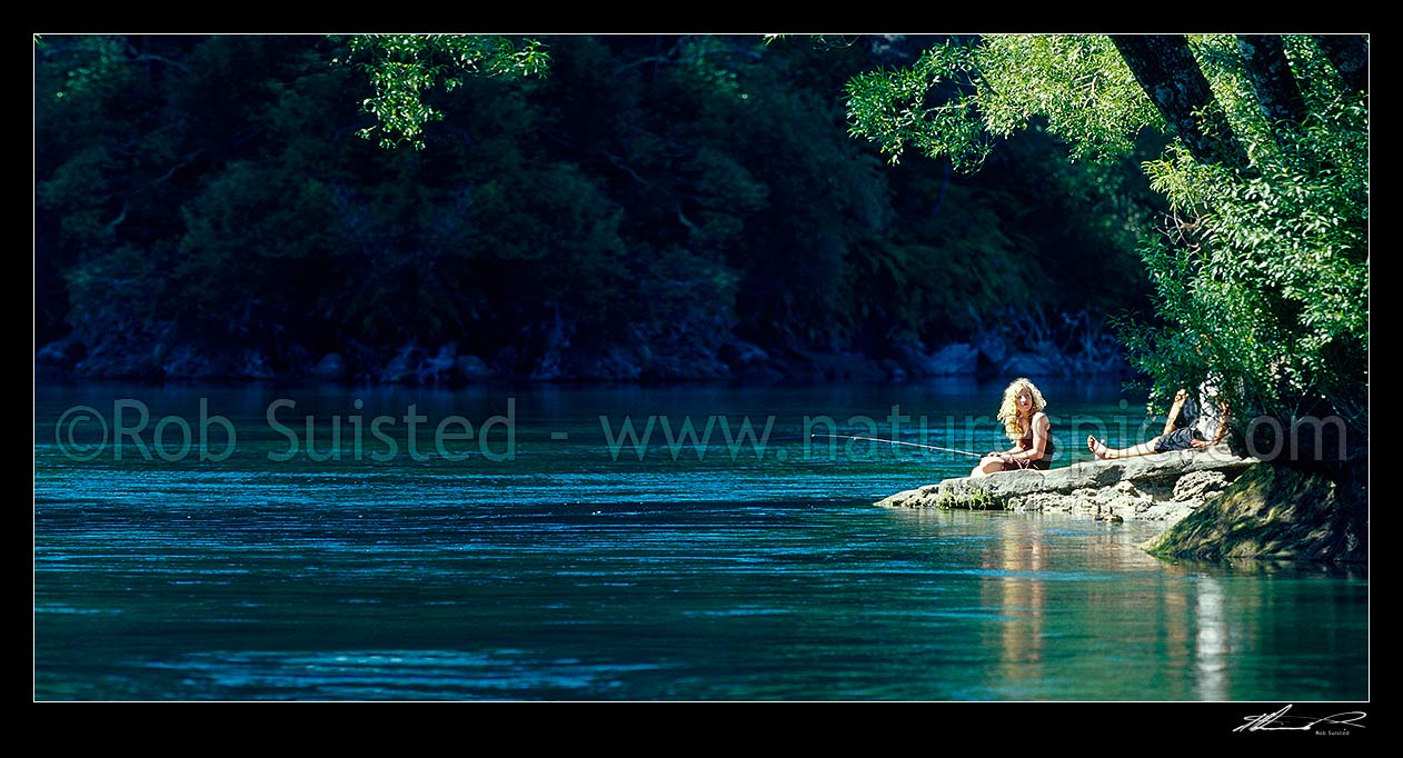 Image of Relaxing sunny summer's day fishing on the Waikato River. Young woman and friend trout fishing under willow trees. Panorama, Taupo, Taupo District, Waikato Region, New Zealand (NZ) stock photo image