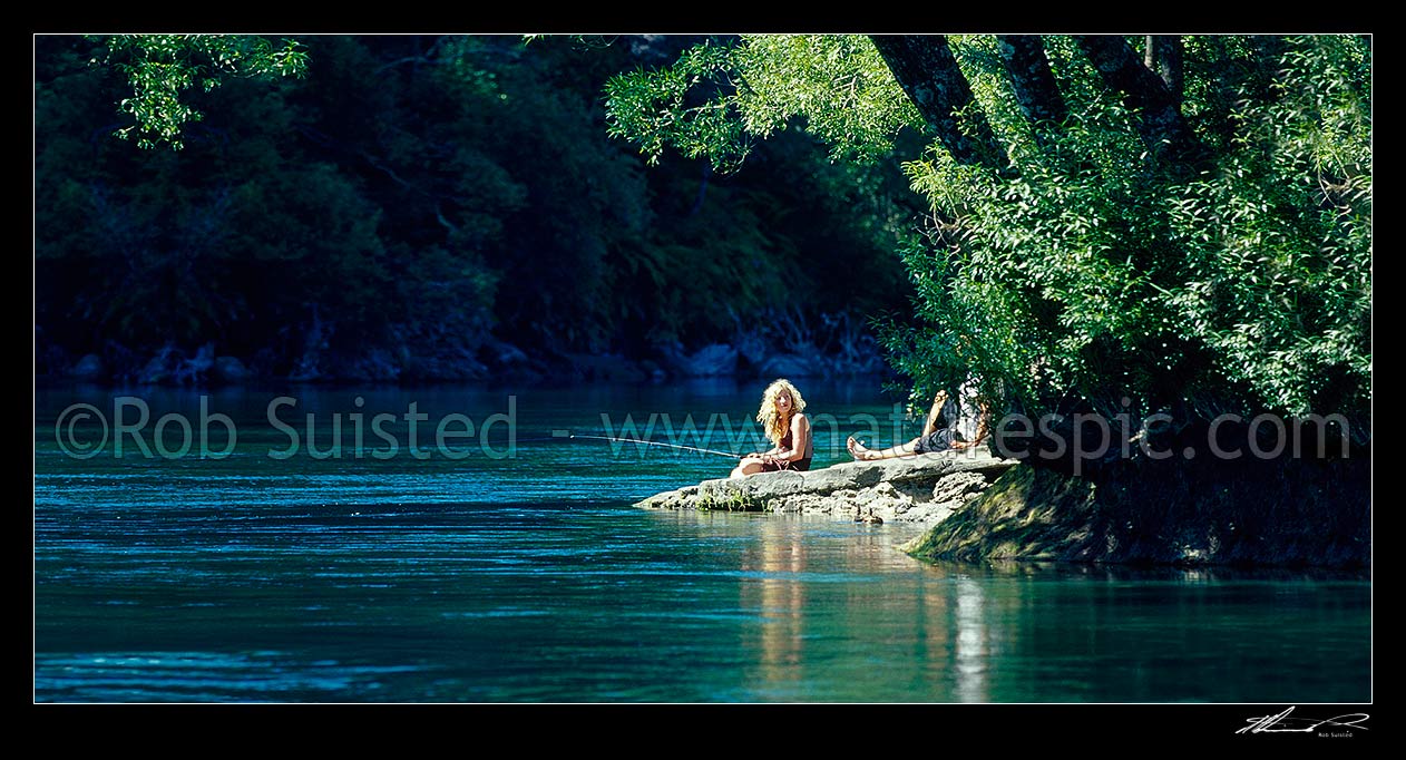 Image of Relaxing sunny summer's day fishing on the Waikato River. Young woman and friend trout fishing under willow trees. Panorama, Taupo, Taupo District, Waikato Region, New Zealand (NZ) stock photo image