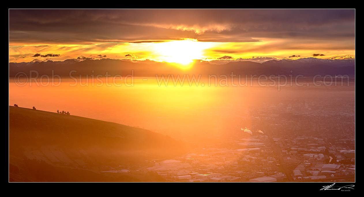 Image of Sunset over Christchurch City. Sun setting behind the Southern Alps. Seen from The Port Hills. Panorama, Christchurch, Christchurch City District, Canterbury Region, New Zealand (NZ) stock photo image