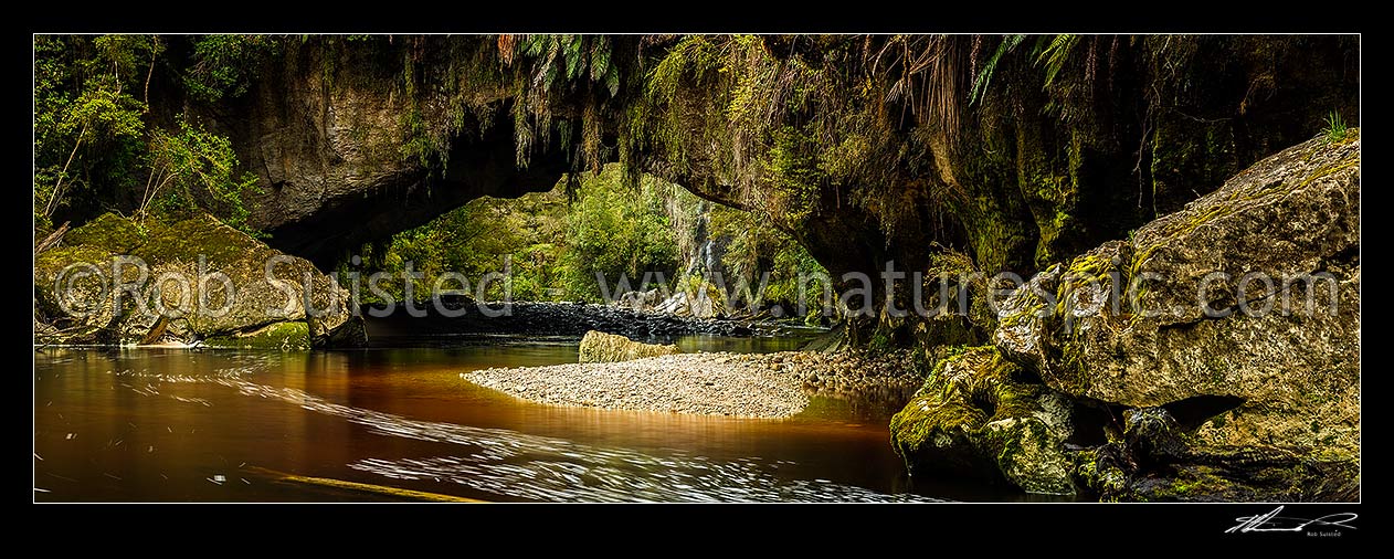 Image of Oparara Arch. The Oparara River entering the little Oparara arch (Moria Gate). Clean, dark vegetation and tanin stained water moving slowly under the limestone arch. Panorama, Karamea,Kahurangi National Park, Buller District, West Coast Region, New Zealand (NZ) stock photo image