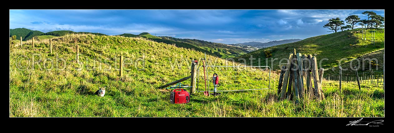 Image of Fencing. Rural fencer building a new post and batten 8 wire fence and hanging new gate, with power generator and fencing tools. Dog watching on. Panorama, New Zealand (NZ) stock photo image