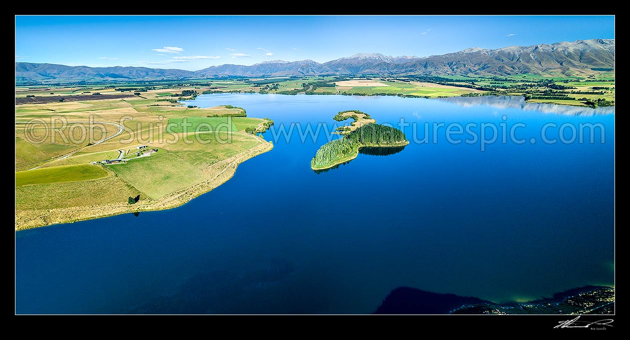 Image of Lake Opuha and island, a man made lake for irrigation and power generation, with Sherwood Range beyond lush green farmland around Ashwick Flat. Aerial view, Fairlie, MacKenzie District, Canterbury Region, New Zealand (NZ) stock photo image