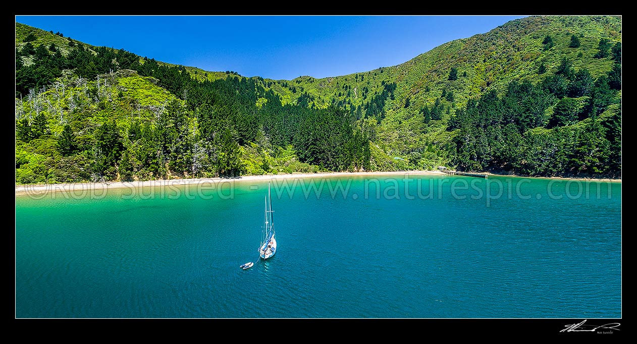 Image of Wharehunga Bay and Wharehunga Beach, historical site from Captain Cook's visits. Aerial panorama in Queen Charlotte Sound, with visiting yacht in bay, Arapawa Island, Marlborough Sounds, Marlborough District, Marlborough Region, New Zealand (NZ) stock photo image