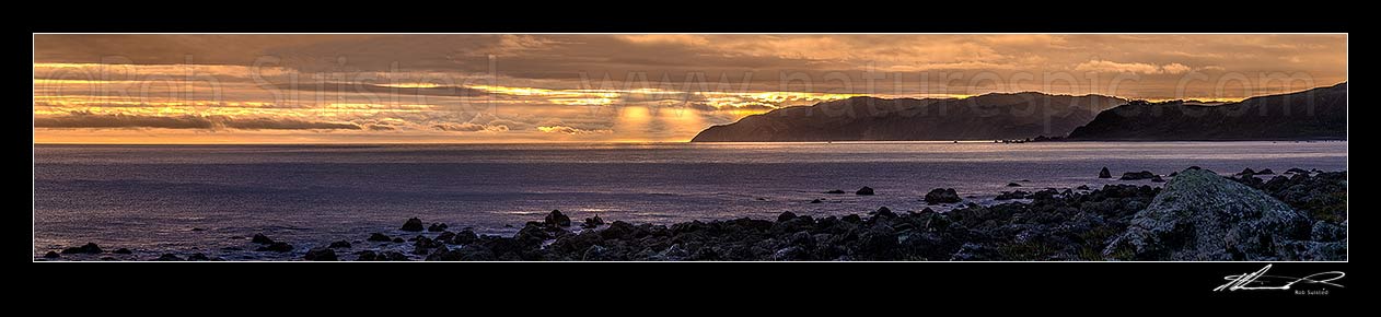 Image of Wellington South Coast and Cook Strait with spectactular light show at sunset over Sinclair Head (centre). Baring Head at right. Wide panorama, Turakirae Head, Hutt City District, Wellington Region, New Zealand (NZ) stock photo image