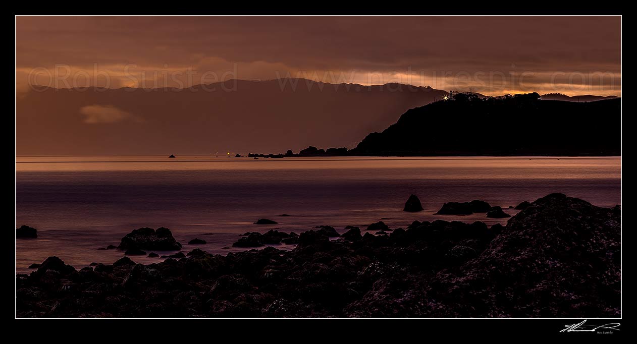 Image of Baring Head lighthouse shining out over Cook Strait from Wellington harbour entrance at twilight. Seen from Turakirae Head Scientific Reserve, Turakirae Head, Hutt City District, Wellington Region, New Zealand (NZ) stock photo image