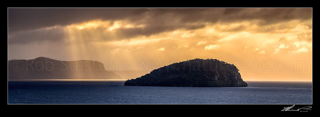 Image of Lake Taupo with moody weather breaking. Motutaiko Island in Lake Taupo (Taupomoana). Crepuscular rays on the western lake shore cliffs of Karangahape behind. Panorama, Motutere, Taupo District, Waikato Region, New Zealand (NZ) stock photo image