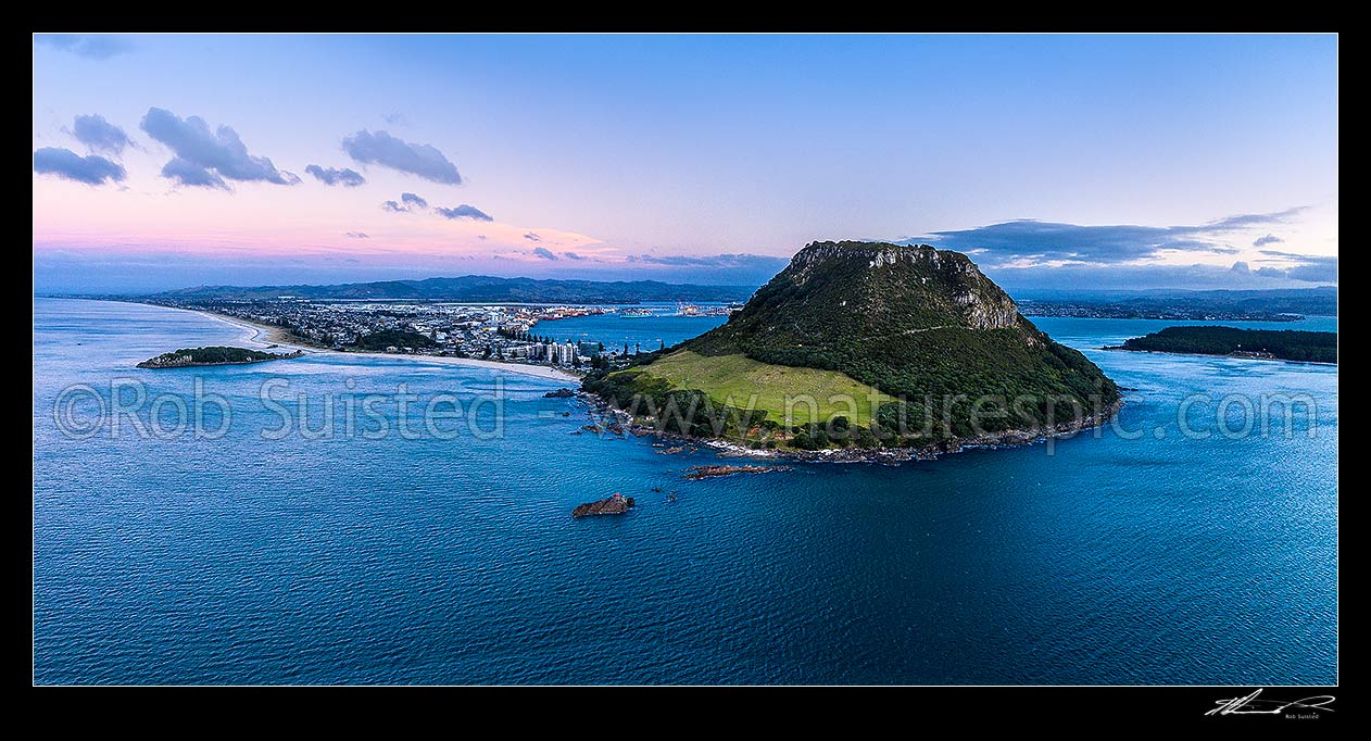 Image of Mount Maunganui, or Mauao, at the Tauranga Harbour Entrance. 231m high lava dome. Moturiki Island at left, Tauranga Port cenre, City right. Aerial view at dusk, Mount Maunganui, Tauranga District, Bay of Plenty Region, New Zealand (NZ) stock photo image