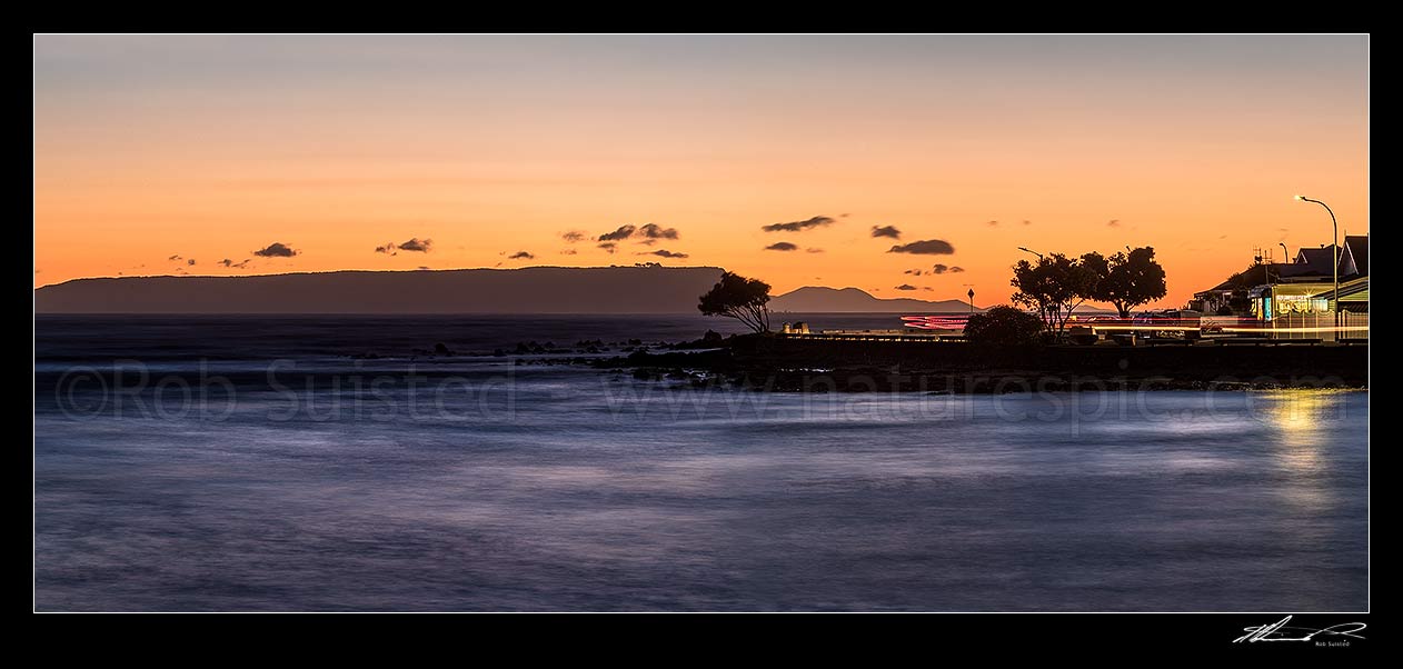 Image of Plimmerton Beach sunset, looking towards Mana Island, with traffic moving on Sunset Parade at dusk. Panorama, Plimmerton, Porirua City District, Wellington Region, New Zealand (NZ) stock photo image