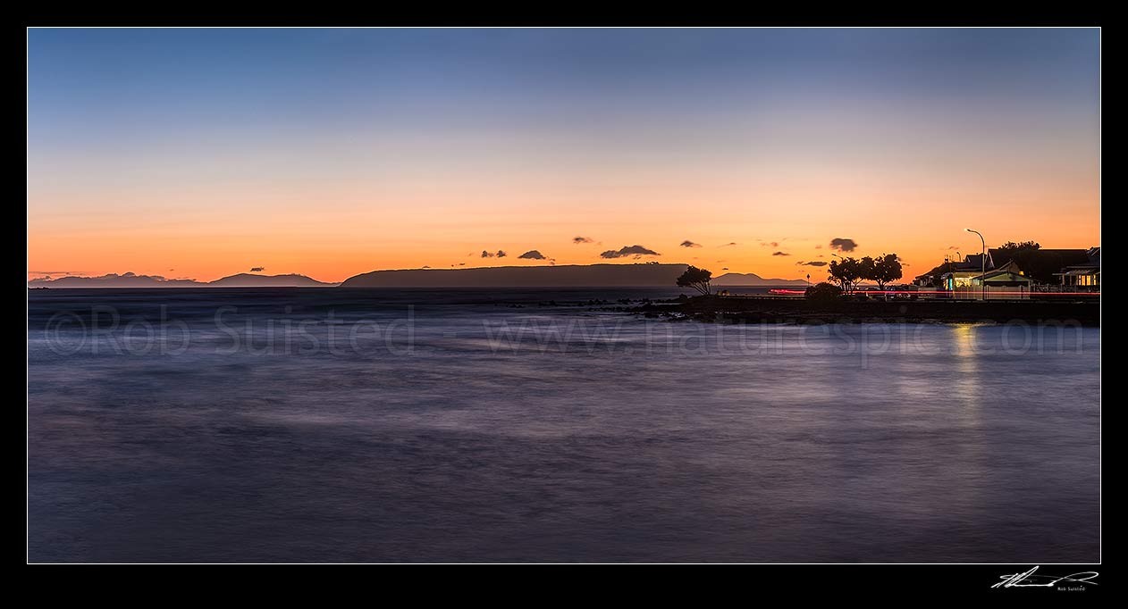 Image of Plimmerton Beach sunset with traffice moving on Sunset Parade road. Mana Island centre, and South Island in distance. Panorama, Plimmerton, Porirua City District, Wellington Region, New Zealand (NZ) stock photo image