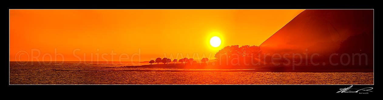 Image of Mahia Peninsula coastal sunrise at Kahutara Point (Table Cape), with sun rays through trees and morning sea mist. Wide panorama, Mahia, Wairoa District, Hawke's Bay Region, New Zealand (NZ) stock photo image