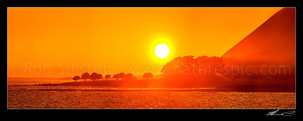 Image of Mahia Peninsula coastal sunrise at Kahutara Point (Table Cape), with sun rays through trees and morning sea mist. Panorama, Mahia, Wairoa District, Hawke's Bay Region, New Zealand (NZ) stock photo image