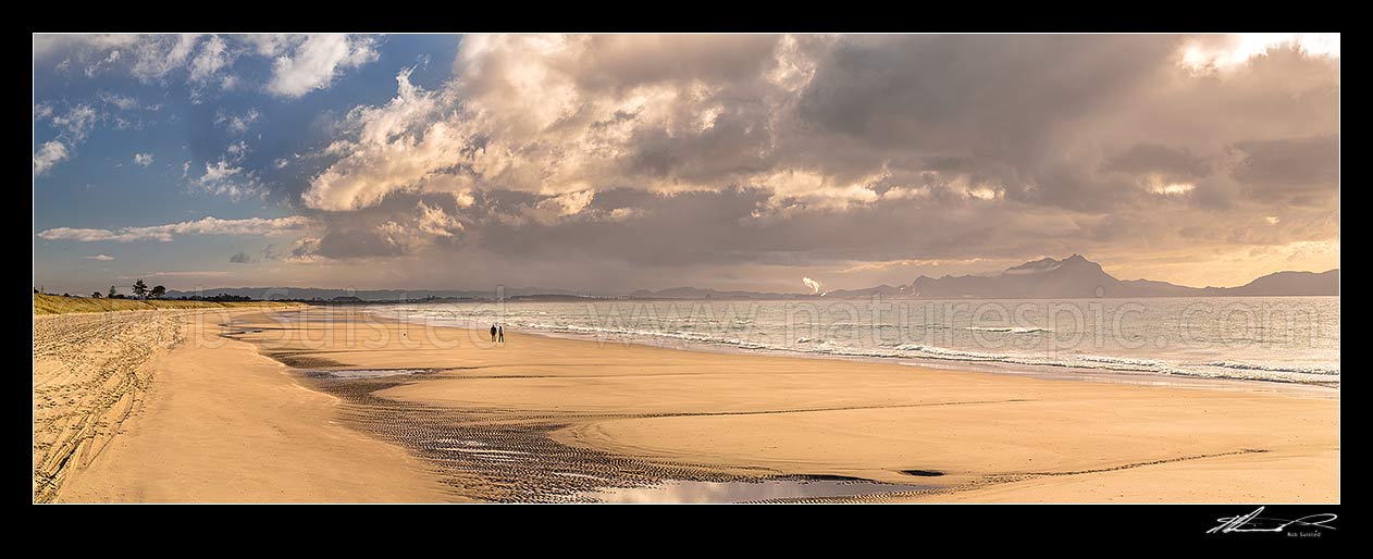 Image of Ruakaka Beach panorama, with people walking in evening light. Mt Manaia (right, 420m) behind right, at the Whangarei Harbour Heads, Ruakaka, Whangarei District, Northland Region, New Zealand (NZ) stock photo image