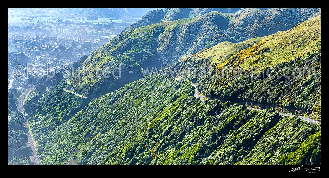 Image of Paekakariki Hill Road winding up the Paekakariki escarpment. Panorama over farmland and regenerating native forest. Paekakariki and main truck railway line far left, Paekakariki, Kapiti Coast District, Wellington Region, New Zealand (NZ) stock photo image