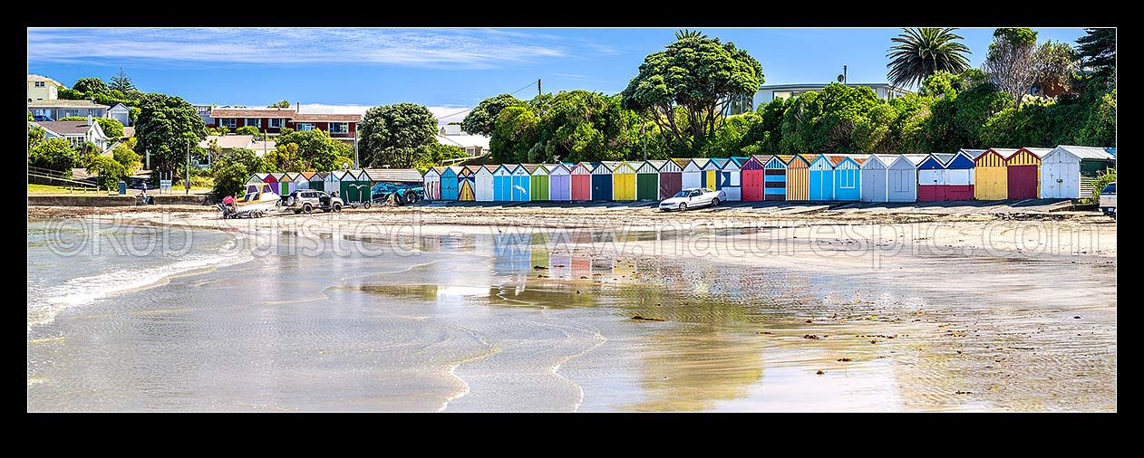 Image of Titahi Bay boatsheds, iconic brightly painted sheds on Titahi Bay beach front, north end, with boat about to be launched. Panorama, Titahi Bay, Porirua City District, Wellington Region, New Zealand (NZ) stock photo image