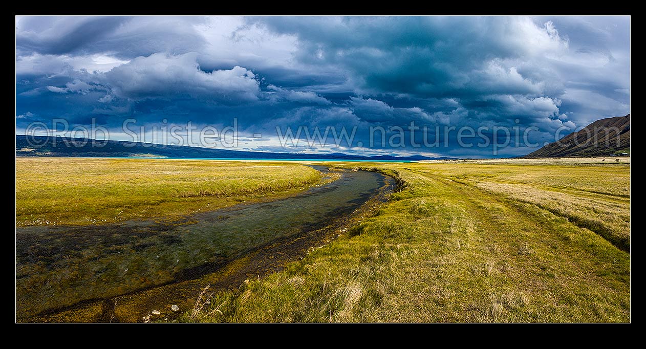 Image of Lake Pukaki's turquoise blue waters under a heavy brooding sky. Lake Pukaki lake shore and edge in the Tasman Valley where a spring fed creek passes. Panorama, Lake Pukaki, MacKenzie District, Canterbury Region, New Zealand (NZ) stock photo image