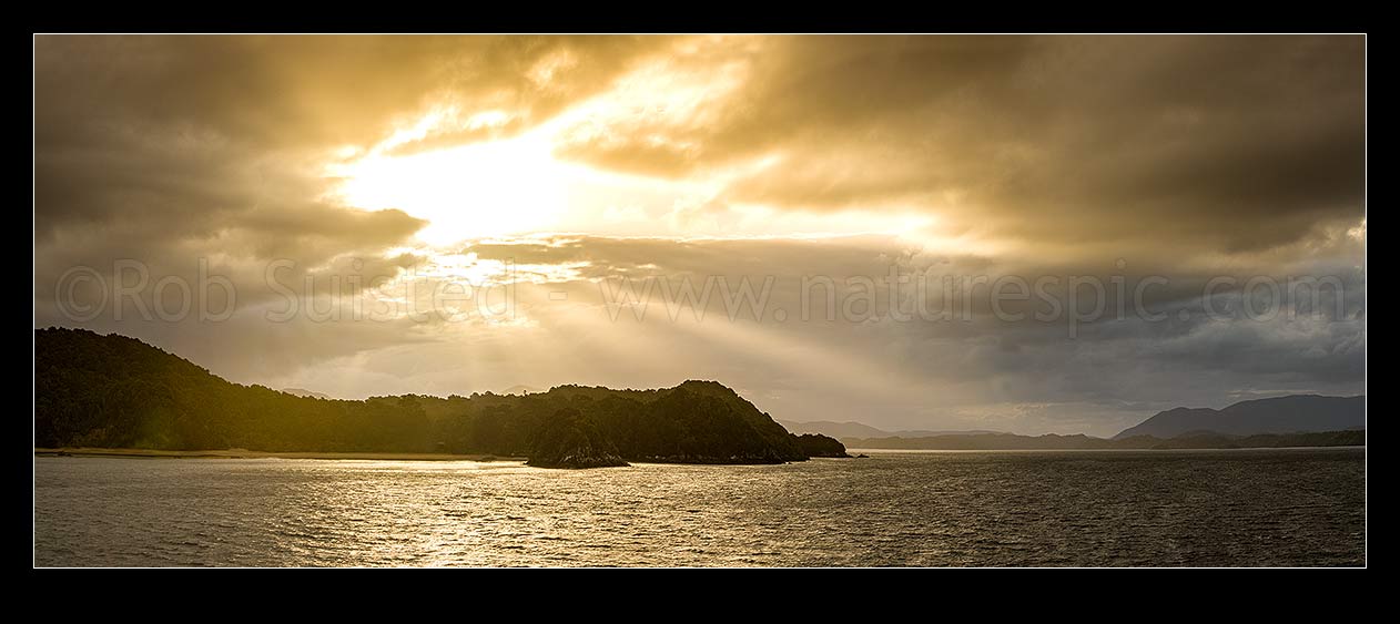 Image of Sunlit rays over Paterson Inlet Whaka a Te Wera. Evening crepusular rays and glowing skies lighting Ulva Island at left. Rakiura panorama, Paterson Inlet, Stewart Island District, Southland Region, New Zealand (NZ) stock photo image